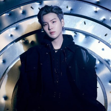 Em fundo metalizado com marcas de bala perdida, SUGA está vestido de preto olhando fixamente para a câmera.