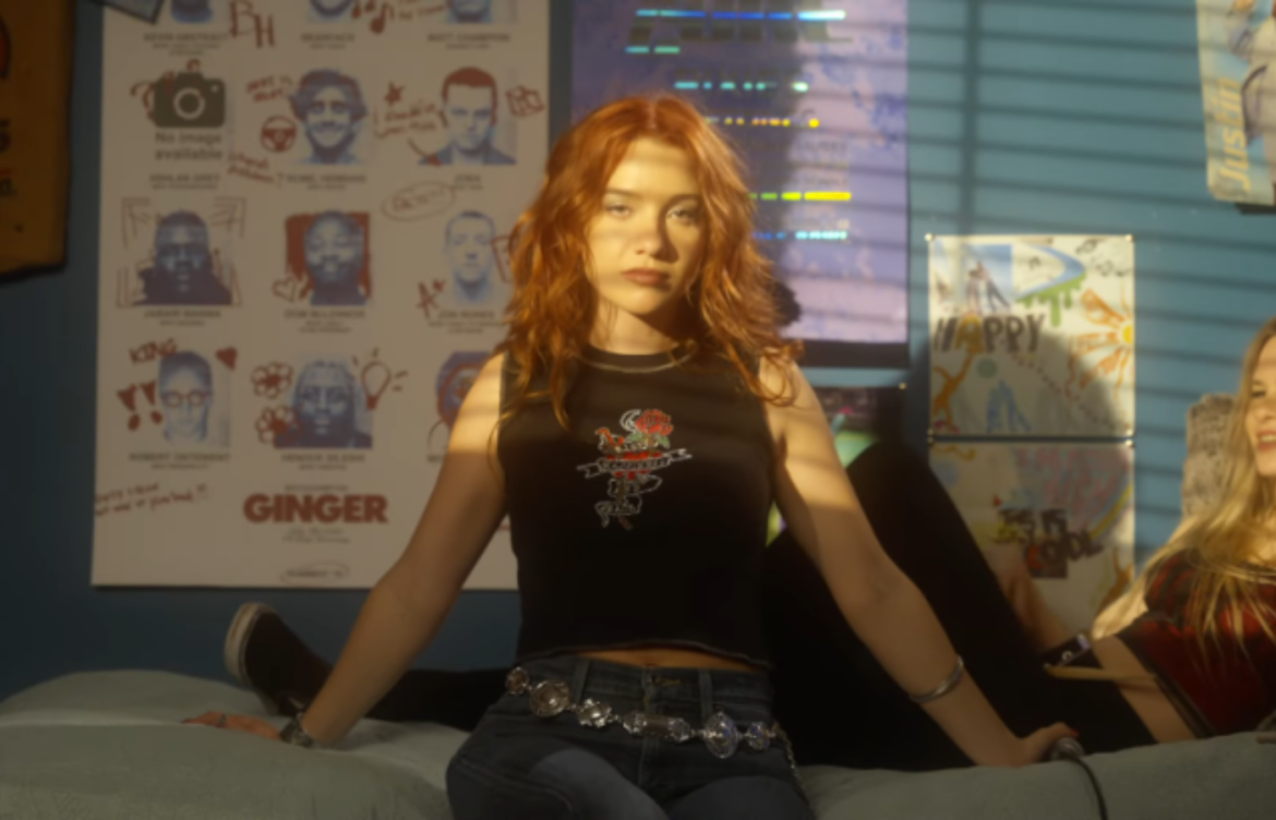 Linsey Urrea sentada em uma cada de um cenário de um quarto encarando a cãmera