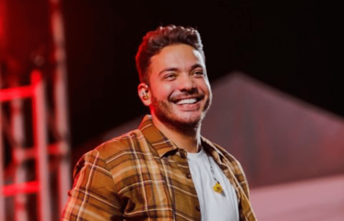 Wesley Safadão sorri para o público em cima de um palco.