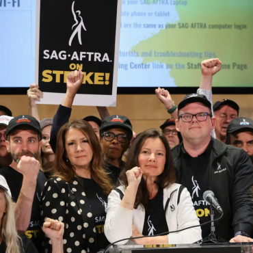 Diversos atores erguem a mão para cima em foto do momento que anuncia greve de atores.