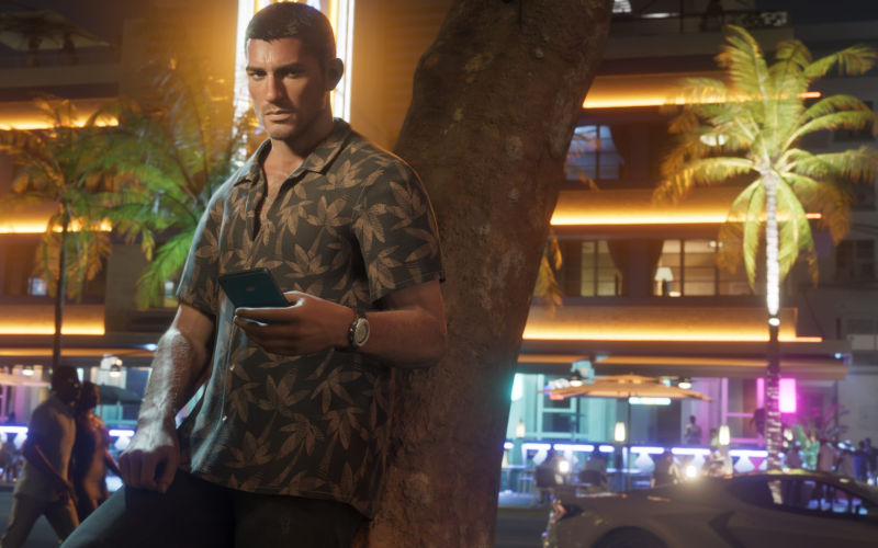 Personagem masculino de GTA 6 encostado em uma árvore no coração vibrante de Vice City, à noite, com expressão séria e celular na mão, em meio ao clima tropical e luzes neon da cidade.