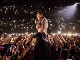 Chester Bennington, vocalista do Linkin Park, canta sem camisa em meio ao público durante show lotado, com milhares de luzes de celulares acesas iluminando a plateia.