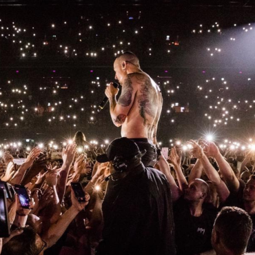Chester Bennington, vocalista do Linkin Park, canta sem camisa em meio ao público durante show lotado, com milhares de luzes de celulares acesas iluminando a plateia.