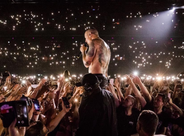 Chester Bennington, vocalista do Linkin Park, canta sem camisa em meio ao público durante show lotado, com milhares de luzes de celulares acesas iluminando a plateia.