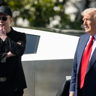 Elon Musk e Donald Trump em frente a uma caminhonete Cybertruck; Musk usa boné "Make America Great Again" e está com os braços cruzados, enquanto Trump veste terno azul com gravata vermelha.