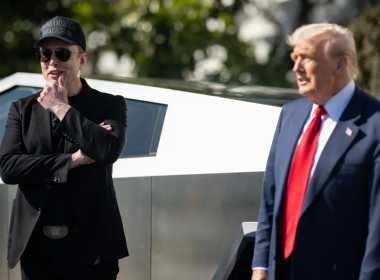 Elon Musk e Donald Trump em frente a uma caminhonete Cybertruck; Musk usa boné "Make America Great Again" e está com os braços cruzados, enquanto Trump veste terno azul com gravata vermelha.