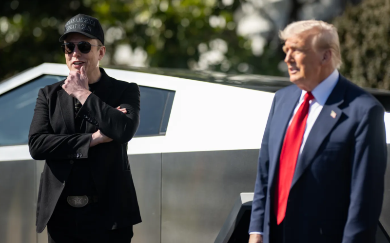 Elon Musk e Donald Trump em frente a uma caminhonete Cybertruck; Musk usa boné "Make America Great Again" e está com os braços cruzados, enquanto Trump veste terno azul com gravata vermelha.